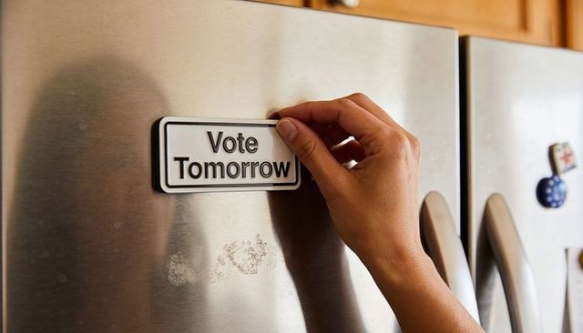 Hand placing vote tomorrow magnet on stainless refrigerator door showing civic reminder