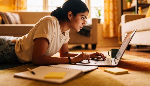 Indian woman typing on laptop in cozy sunlit living room studying and working from home