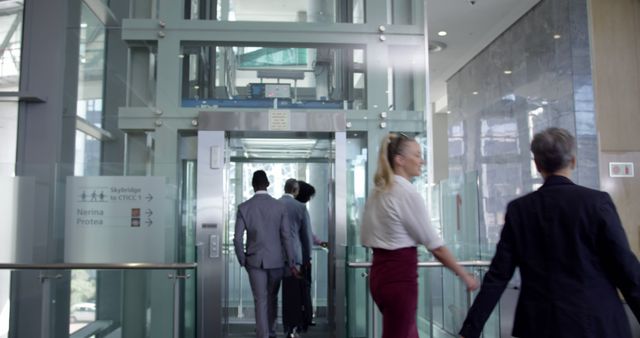 Business professionals in business attire entering glass elevator in a modern corporate building. Ideal for illustrating corporate environments, teamwork, diversity in the workplace, and modern office settings.