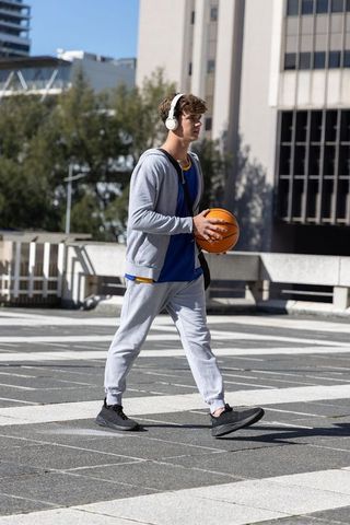 Teen walking while holding basketball and listening on headphones in urban plaza