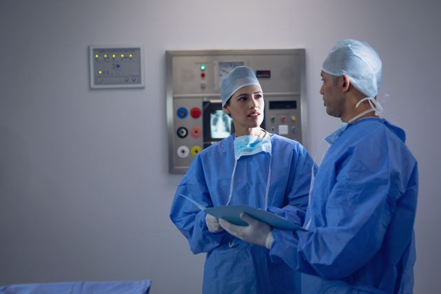 Surgeons in blue scrubs and surgical caps are discussing a medical file in an operating room. This image can be used for healthcare, medical teamwork, hospital environments, and surgical procedures. Ideal for medical websites, healthcare blogs, and educational materials.
