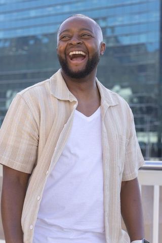 Laughing african american man leaning on balcony by glass facade urban rooftop sunlit