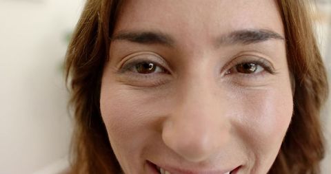 Close-up smiling mid-adult woman showing natural skin texture, fine lines, brown eyes