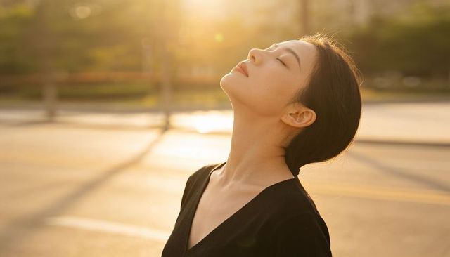 Sunlit serenity asian woman tilting face to golden light, tranquil outdoor portrait