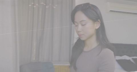 Standing woman wearing fitted long-sleeve top and sunglasses on head in soft bedroom light
