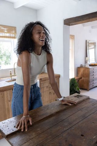 Laughing african american woman leaning on rustic wooden island in farmhouse kitchen