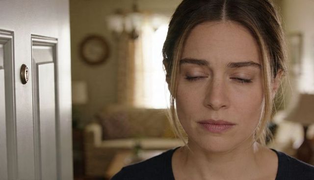 Contemplative woman standing by door with eyes closed, calm interior home moment