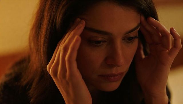 Young woman holding temples in warm lamp light closeup, tense intimate headache moment