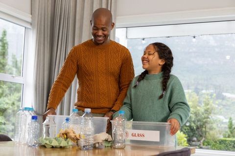 African american father and daughter sorting recyclables at home with labeled glass bin
