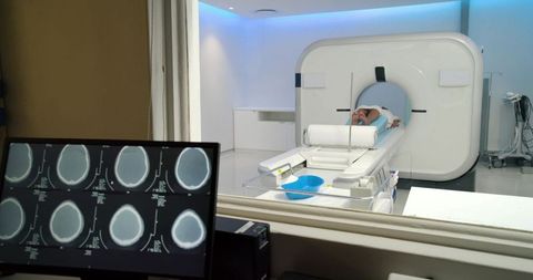 Female patient undergoing ct scan in modern radiology suite with brain scans on monitor
