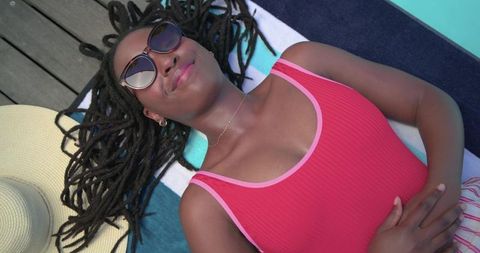 African woman relaxing by pool in red swimsuit and sunglasses, summer leisure and wellness