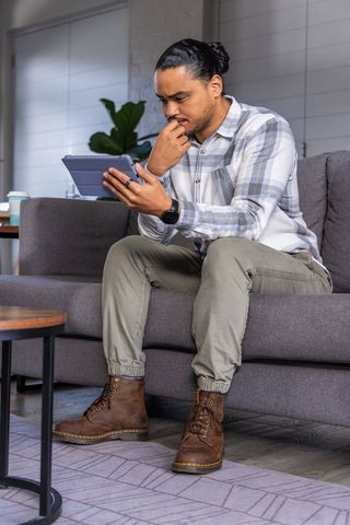 Thoughtful man contemplating while using tablet on gray sofa in modern living room