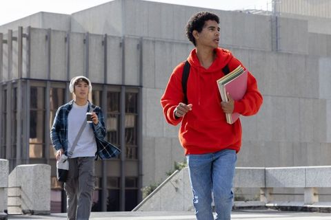 African american and asian students walking urban campus plaza carrying folders, backpacks