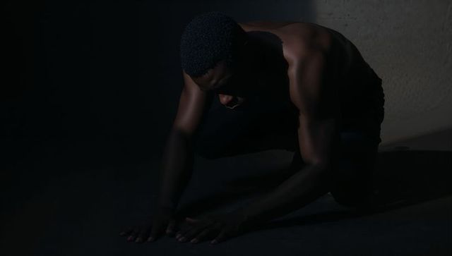 Low-key moody portrait of kneeling shirtless man with sculpted shoulders and deep shadows