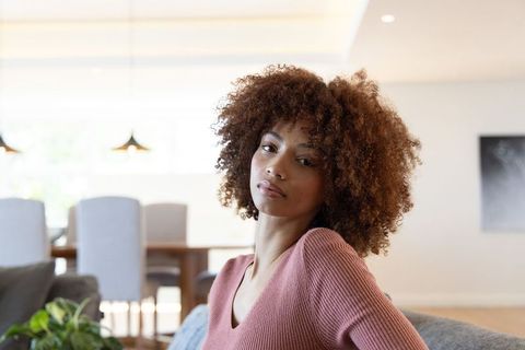 African american woman sitting on sofa in modern living room wearing dusty-rose sweater