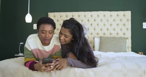 Diverse friends lounging together with smartphone in cozy bedroom