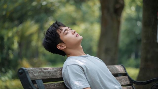 Young Asian Man Reclining on Wooden Park Bench in Sunlit Greenery, Serene Restful Moment