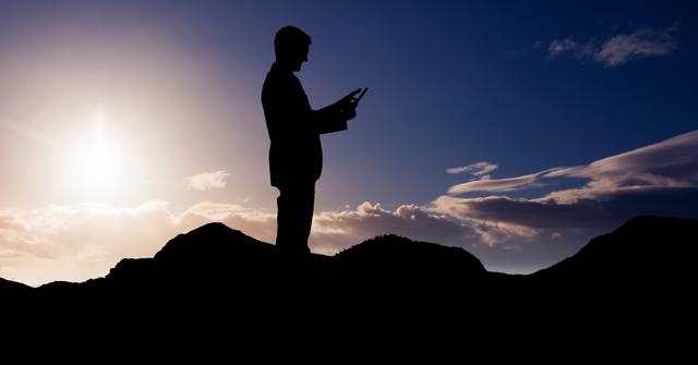 Digital composite of Silhouette businessman using tablet PC on mountain during sunset