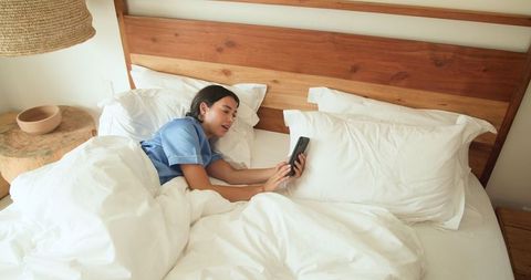 Woman Relaxing in Bed with Smartphone in Cozy Bedroom