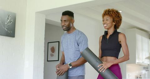 African american couple practicing home yoga with mats and smartwatch in minimalist home