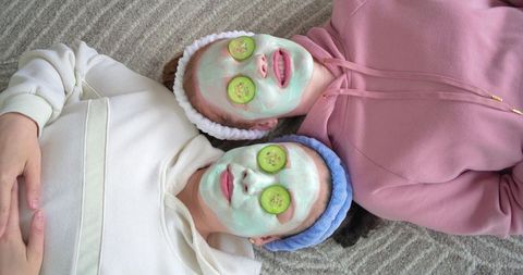 Diverse friends enjoying at-home spa relaxing with green face masks and cucumber slices