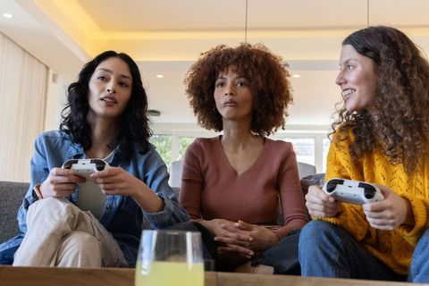 Diverse friends gaming on sofa with white controllers enjoying multiplayer night at home