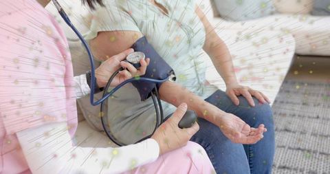 Home nurse measuring blood pressure on patient with cuff and gauge on living room sofa
