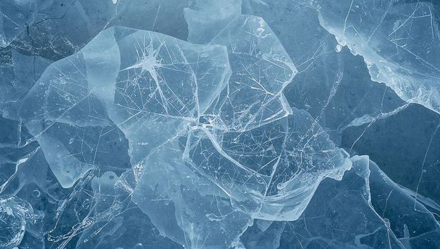 Fractured blue ice plates revealing radial cracks and trapped bubbles on frozen lake