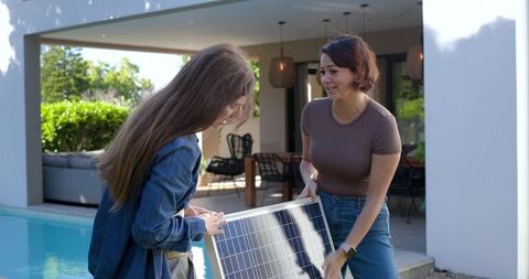 Friends carrying portable solar panel by backyard pool during diy renewable energy project