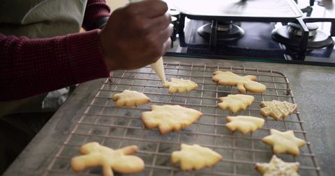 African American man decorating festive cookies on cooling rack in home kitchen