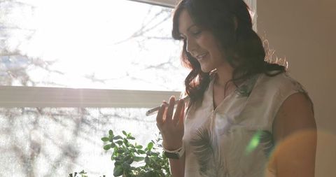 Woman Smiling While Talking on Smartphone by Sunny Window