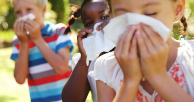 Children are shown in an outdoor setting, using tissues to blow their noses. This depicts a typical scenario during cold or allergy season. Ideal for use in health-related articles, children's hygiene campaigns, pharmaceutical advertisements, and pediatric healthcare materials.