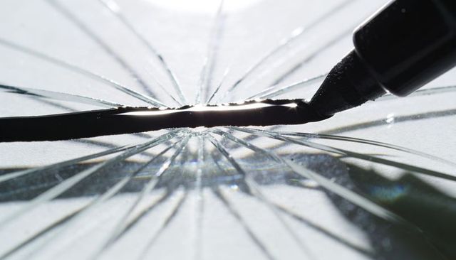 Tracing marker tip along central crack on broken glass with radial fractures and reflections