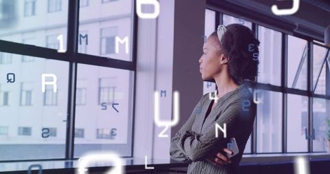 Contemplative Black professional gazing through office windows holding phone with AR overlay