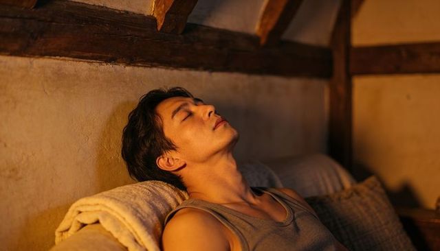 Young man reclining in rustic loft during golden hour resting on daybed with warm blanket