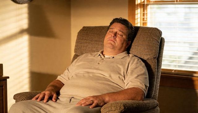 Middle-aged man sleeping in recliner bathed in warm sunlight in cozy living room