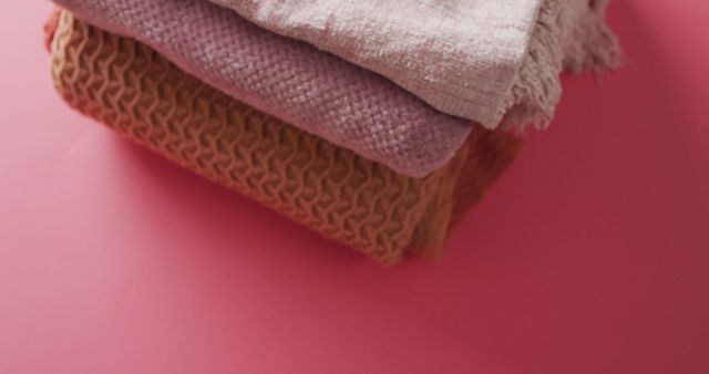 Colorful textiles stacked neatly on a pink surface, showing different textures and fabrics. Ideal for promoting home decor, fabric stores, or textile products. Can be used in blogs, advertisements, or social media posts related to interior design and comfort.