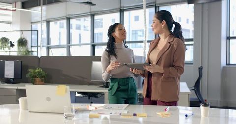 Diverse female coworkers collaborating over tablet and charts in bright modern office