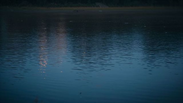 Twilight lake ripples reflecting warm orange lights on calm blue water surface