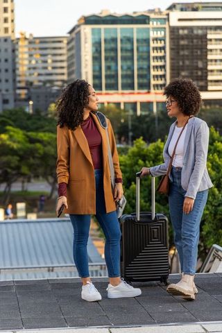 African american friends traveling together chatting on urban promenade with luggage