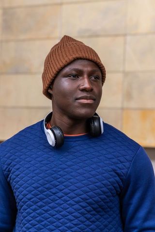 Standing young man wearing brown beanie and headphones in urban minimalist portrait