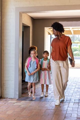 African american guardian walking with school girls through sunlit brick passageway