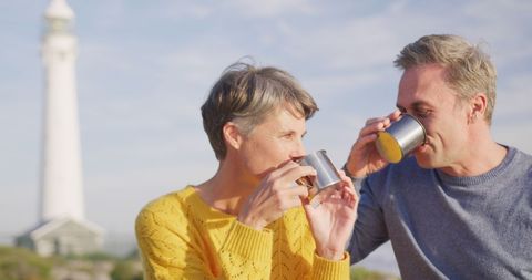Happy Senior Couple Enjoying Coffee Outdoors Near Lighthouse