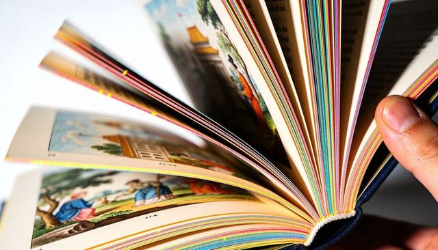 Flipping colorful illustrated hardcover book with rainbow page edges and vintage scenes