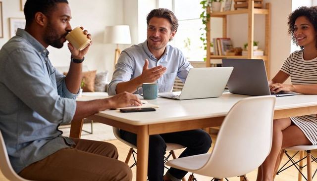 Team Discussing Project Over Coffee in Bright Home Office with Laptops and Casual Attire