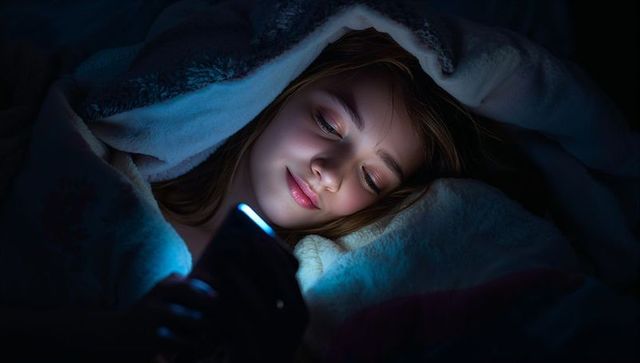Teen girl scrolling on phone under blanket at night