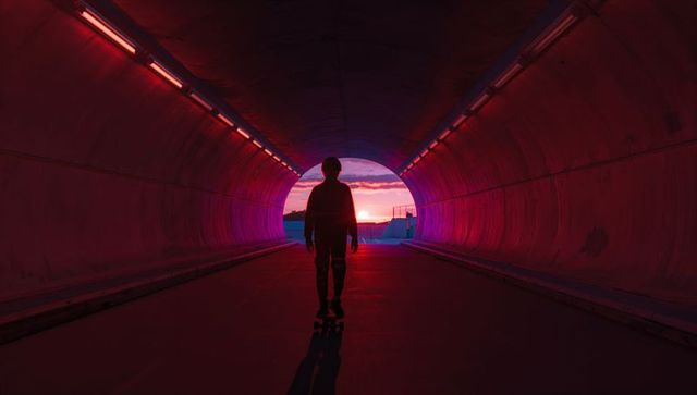 Gliding Silhouetted Skateboarder in Neon Tunnel at Sunset with LED Strip Lighting