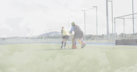 Field hockey attacker charging on turf while goalkeeper blocking shot with pads and helmet
