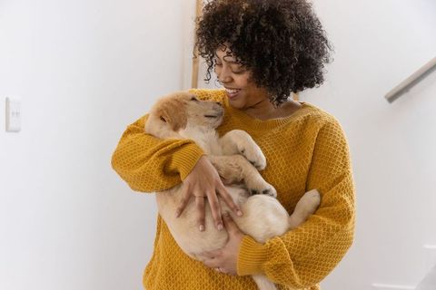 African american woman cradling golden retriever puppy smiling in mustard sweater