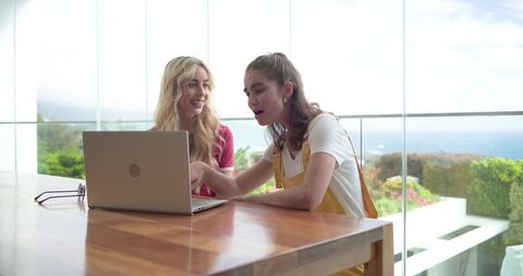 Young women collaborating on laptop at coastal glass terrace with modern minimalist interior